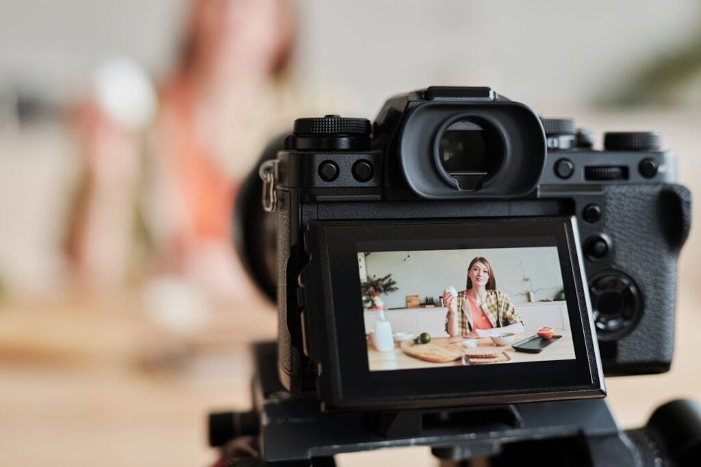 A woman filming a cooking vlog in her kitchen using a digital camera.