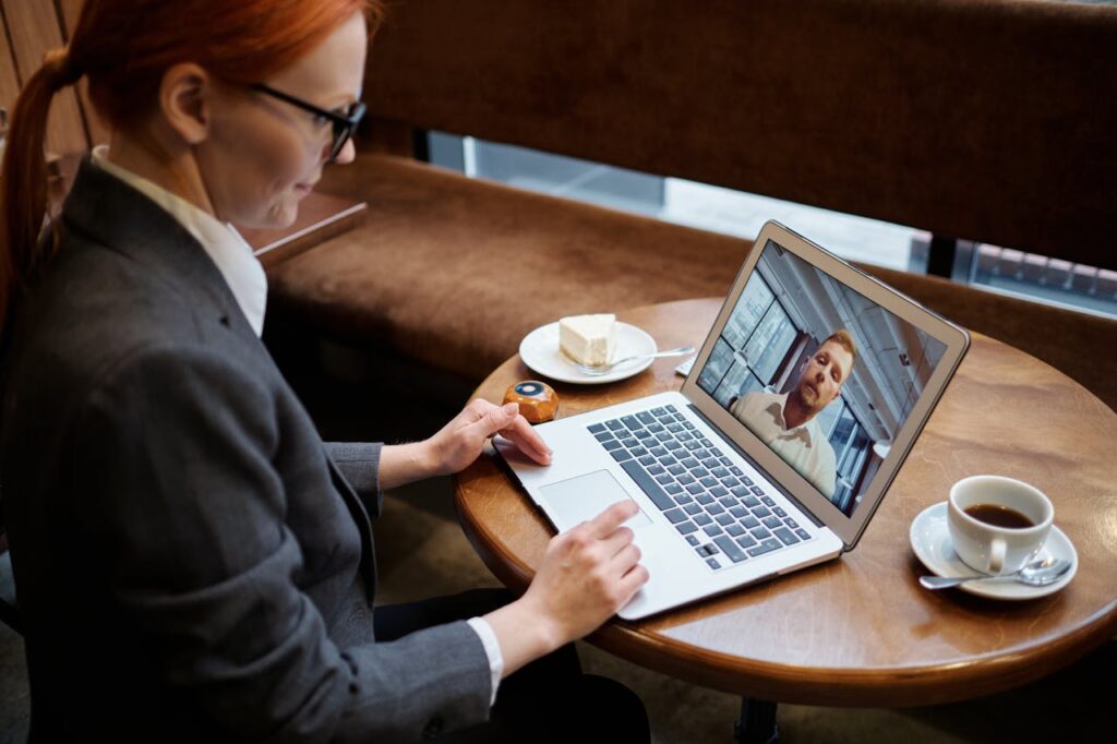 Business woman engaged in a video call meeting in a cozy cafe setting, using a laptop.